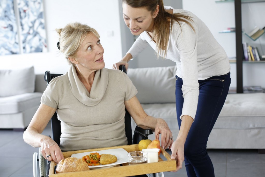 Mladá žena podáva staršej pani na vozíčku podnos s jedlom
